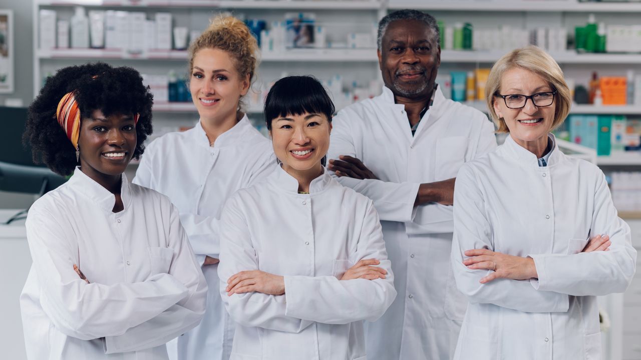 A team of pharmacists smiling together in front of pharmacy shelves