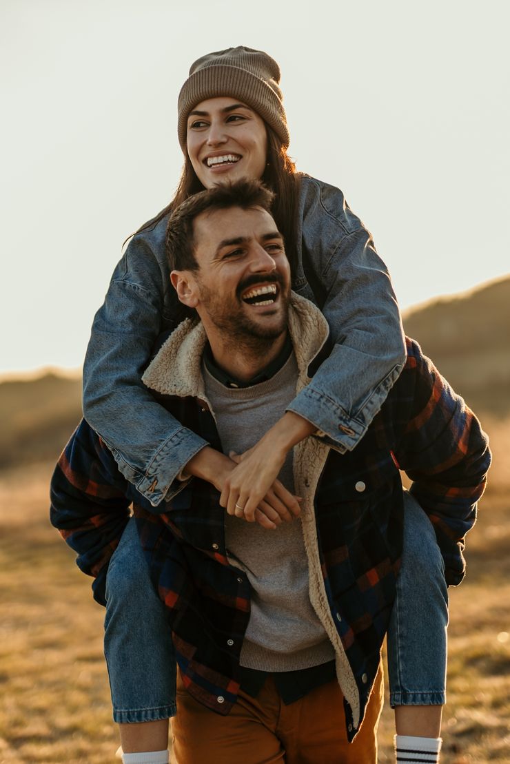 A smiling couple outdoors, the woman on the man's back