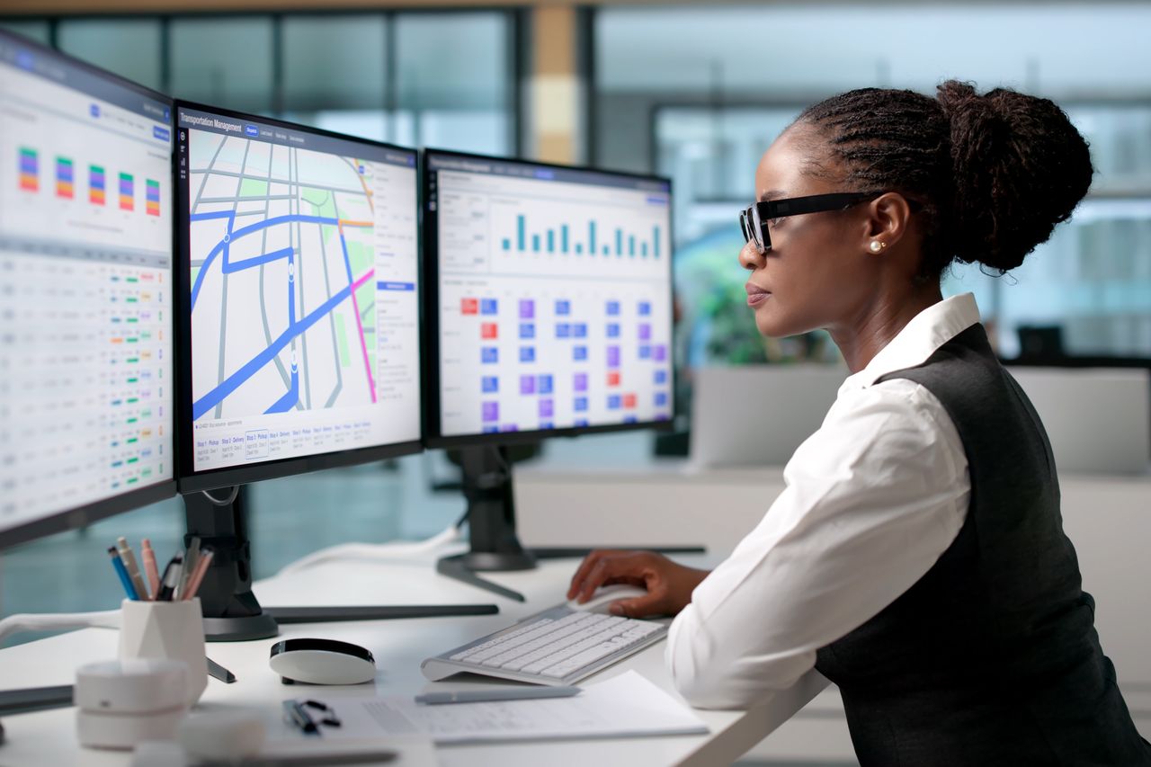 A team member working across three monitors showing pharmacy operations dashboards