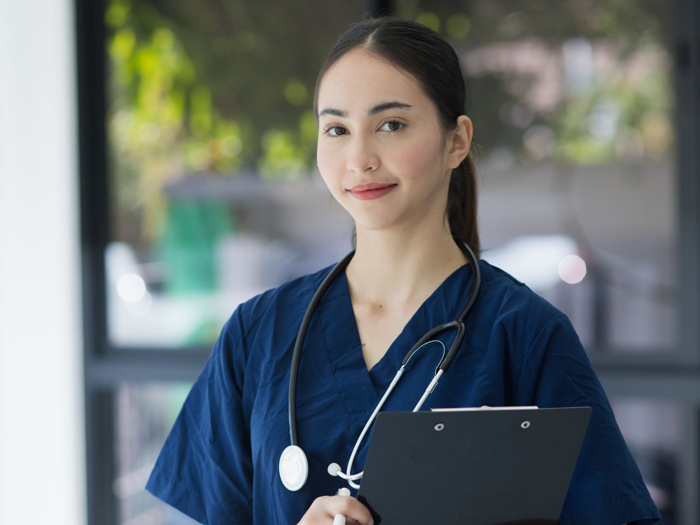 A nurse in scrubs holding a clipboard and smiling