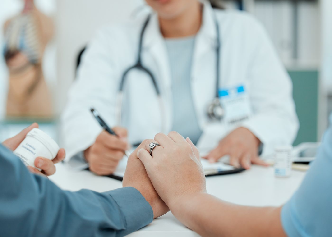 A doctor taking notes while a couple hold hands at a consultation