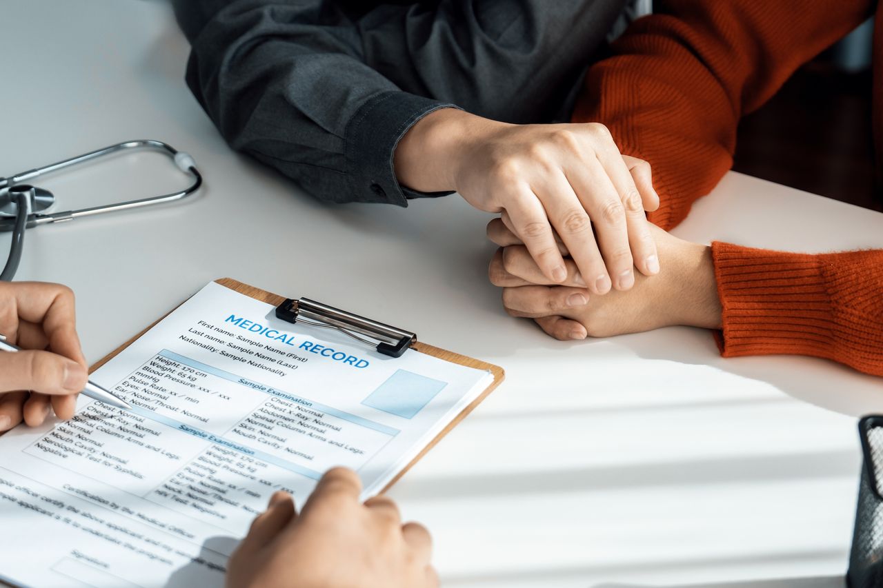 A clinician completing a medical record while a couple hold hands