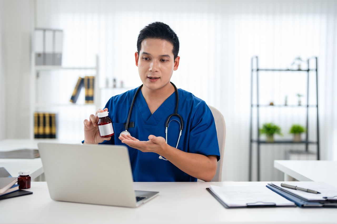 A doctor in scrubs explaining a medicine to a patient at his desk