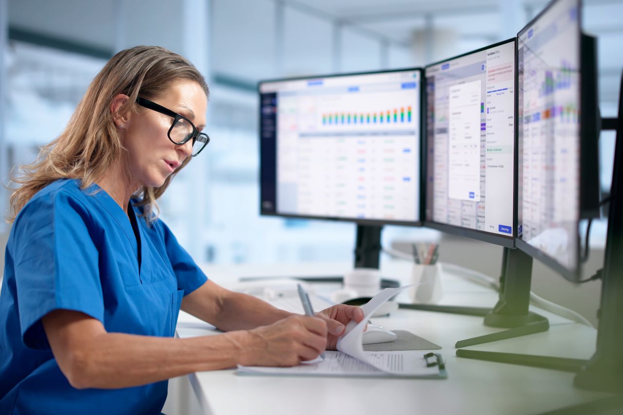 A pharmacist reviewing prescription information on three monitors